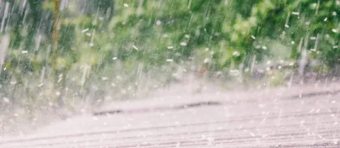 Gros plan d'une très forte pluie tombant en gouttes épaisses sur un toit, avec un flou de verdure en arrière-plan.