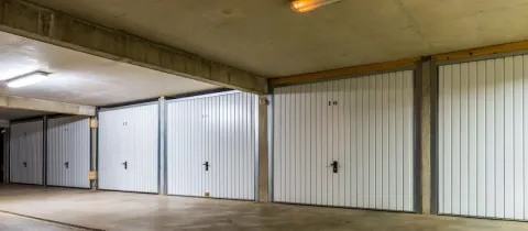 Rangée de boxes de garage individuels, numérotés et fermés par des portes blanches, dans un parking souterrain.