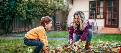 Mère et fils s'amusant à ramasser un tas de feuilles mortes dans le jardin, en automne.