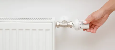Gros plan sur une main ajustant le thermostat d'un radiateur de chauffage central blanc pour réguler la température ambiante.