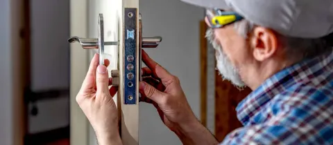 Un serrurier ou un bricoleur barbu répare ou remplace la serrure et la poignée d'une porte intérieure.