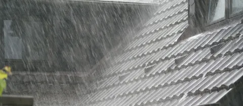 Gros plan sur un toit en tuiles sombres, sous une forte pluie, l'eau s'écoulant par la gouttière.