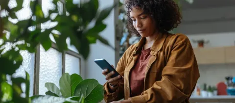 Une femme aux cheveux bouclés prend une photo d'une de ses plantes d'intérieur avec son téléphone.