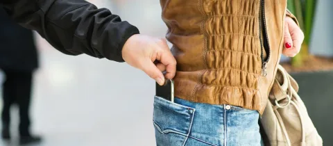 Gros plan d'une main dérobant un smartphone dans la poche arrière du jean d'une personne de manière furtive.