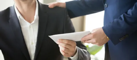 Un homme en costume remet une enveloppe à un autre homme, symbolisant un échange professionnel.