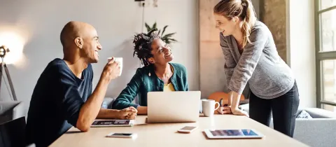 Trois salariés souriants discutent autour d'une table.