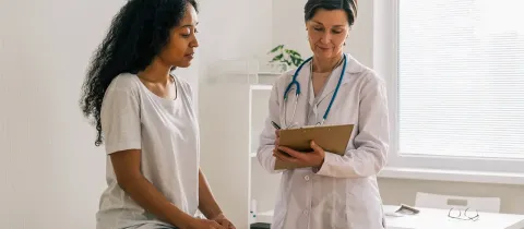 Une médecin en blouse blanche examine une patiente et prend des notes sur un bloc-notes en cabinet médical.