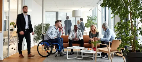 Groupe de collègues discutant de façon inclusive dans un espace de coworking, dont un homme en fauteuil roulant.