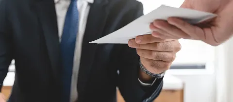Personne en costume tendant une enveloppe à une autre personne.