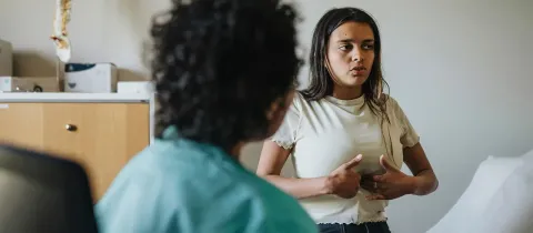 Une patiente assise en consultation médicale montre et explique ses douleurs abdominales à un médecin.
