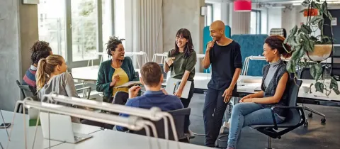Groupe de collègues souriants échangeant de manière conviviale dans un espace de coworking lumineux.