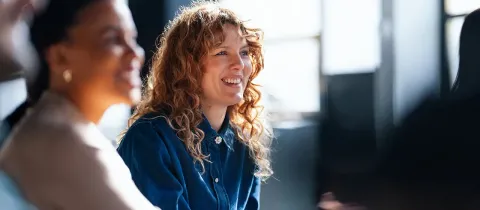 Une femme aux cheveux bouclés sourit chaleureusement lors d'une réunion professionnelle en équipe.