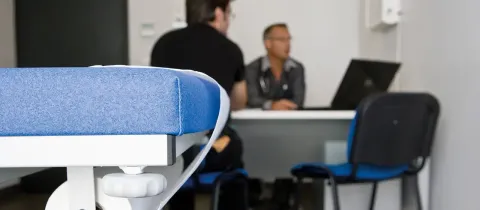 Premier plan sur une table d’examen médicale bleue avec un médecin consultant un patient en arrière-plan.