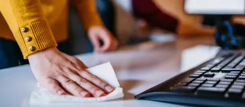 Gros plan sur une main nettoyant un bureau blanc avec un chiffon à côté d'un clavier d'ordinateur noir.
