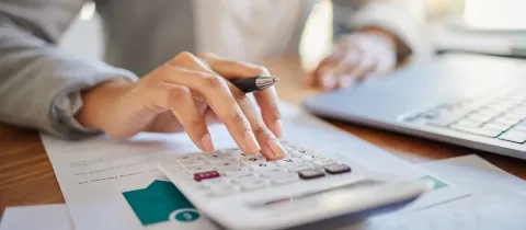 Gros plan sur les mains d'une personne utilisant une calculatrice de bureau pour faire des comptes.