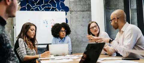 Réunion d'équipe dans un bureau moderne avec plusieurs collaborateurs échangeant autour d'une grande table en bois.