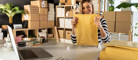 Entrepreneuse souriante préparant une grande enveloppe d'expédition dans son atelier.
