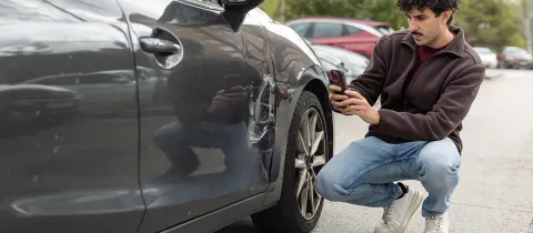 Homme accroupi examinant l'état d'une voiture de fonction