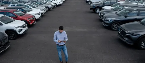 Homme consultant une tablette au milieu d'un parking rempli de véhicules alignés