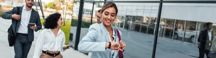 Groupe de collègues de travail en train de partir du travail. La femme au premier plan regarde sa montre.