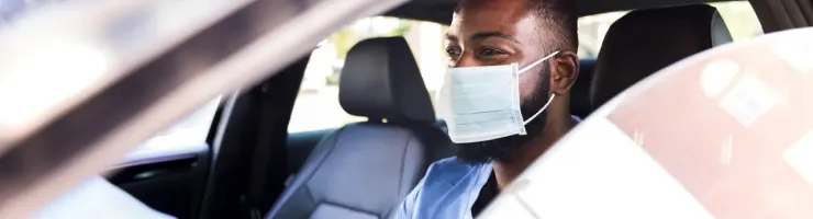 Conducteur portant un masque dans une voiture, respectant les consignes sanitaires.