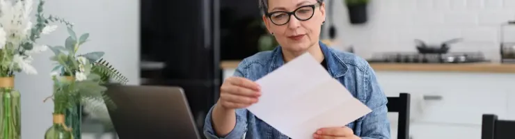 Une femme, assise sur une chaine, lit un document dans sa cuisine