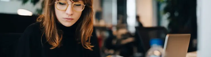 Une femme est en train de consulter son téléphone portable et écrire quelques chose sur une feuille. 