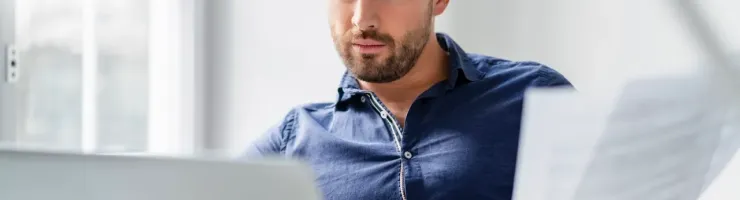 Un homme consulte des documents devant son ordinateur portable, concentré sur ses tâches administratives.