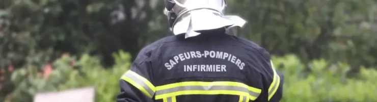 Un pompier vu de dos marche dans une zone boisée, équipement de secours complet.