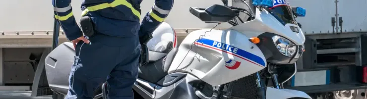 Un policier en uniforme se tient près de sa moto, prêt à intervenir sur la route.