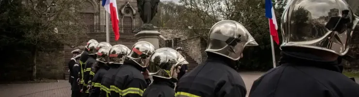 Des pompiers en uniforme, drapeaux français en berne