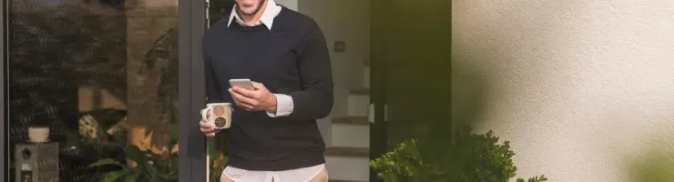 Un homme sort d’un immeuble, tenant un smartphone et une tasse de café.