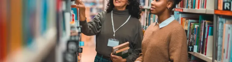Une bibliothécaire et une étudiante discutent ensemble dans une bibliothèque.