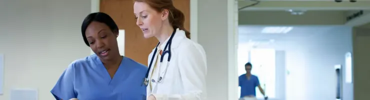 Deux soignantes discutent dans un couloir d’hôpital.