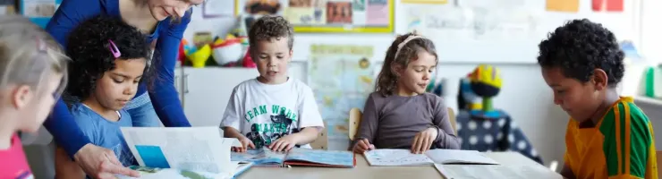 Une maitresse d'école aide une jeune fille à trouver une page d'un livre.