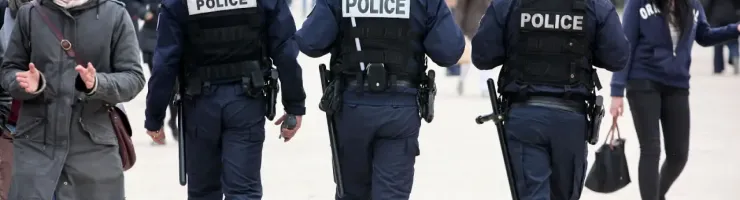 Trois policiers en uniforme marchent dos à la caméra dans un espace public fréquenté.