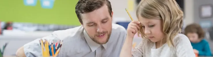 Adulte aide enfant concentré travaillant sur une feuille à un bureau en classe.