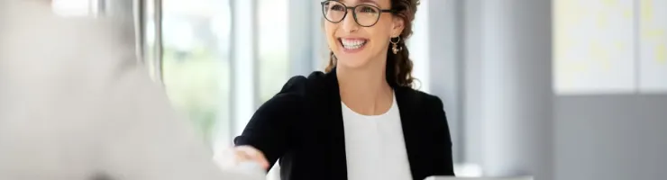 Femme souriante en costume noir accueille un visiteur avec une poignée de main.