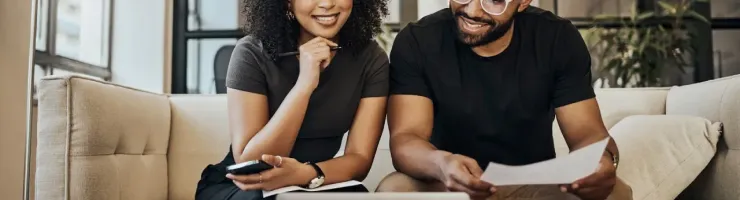 Un homme et une femme souriants sur un canapé regardant un ordinateur portable et des documents.