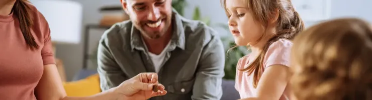 Famille souriante partageant un moment autour d’une table. Les parents éduquent leur fille sur l'épargne en mettant une pièce dans un bocal.