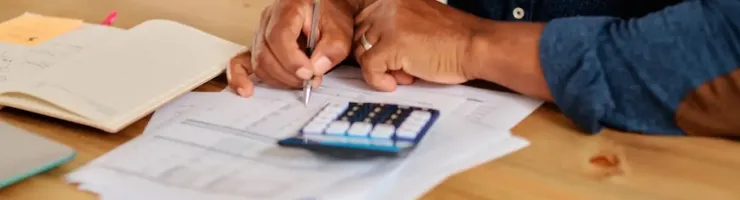 Une femme fait ses comptes en inscrivant les résultats obtenus avec une calculatrice.