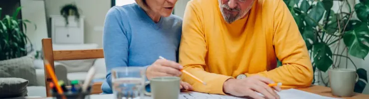 Un couple âgé examine des papiers financiers à table, discutant de leur gestion budgétaire.