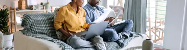 Couple assis sur un canapé, regardant des papiers et un ordinateur portable.