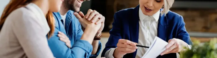 Un couple se fait conseiller par une bancaire. Elle montre des chiffres sur un document.