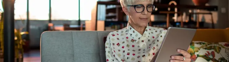 Une femme consulte sa tablette dans son canapé.