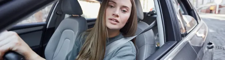 Femme aux longs cheveux blonds assise au volant d'une voiture, regardant par la fenêtre.