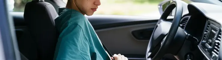Jeune personne assise sur le siège conducteur d'une voiture, attachant sa ceinture de sécurité.
