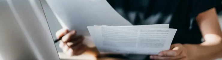 Personne assise à un bureau avec un ordinateur portable, examinant des documents.