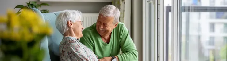 Couple âgé discutant près d'une fenêtre, ambiance chaleureuse.