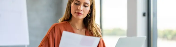 Une femme regarde une feuille et travaille avec un ordinateur portable.